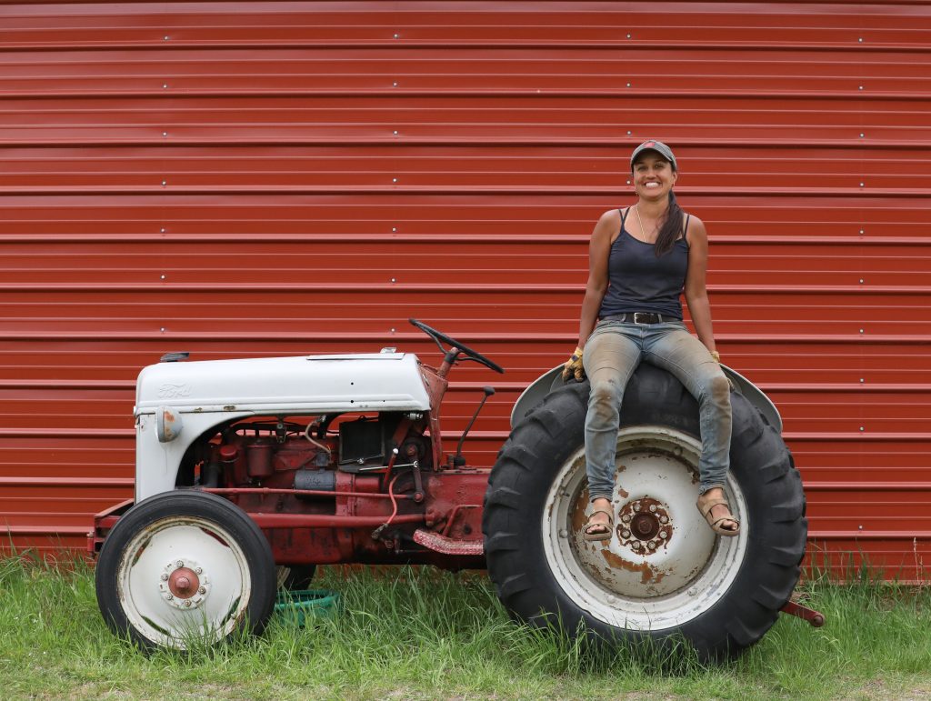 Andal Sundaramurthy sits on the back wheel of her tractor in front of a red garage on her farm